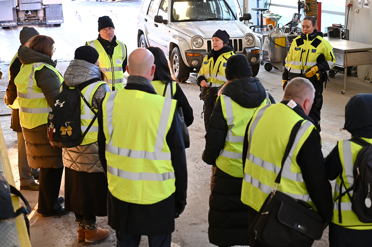 Joukko ihmisiä kerääntynyt puolikaareen kuuntelemaan edessä olevia henkilöitä.