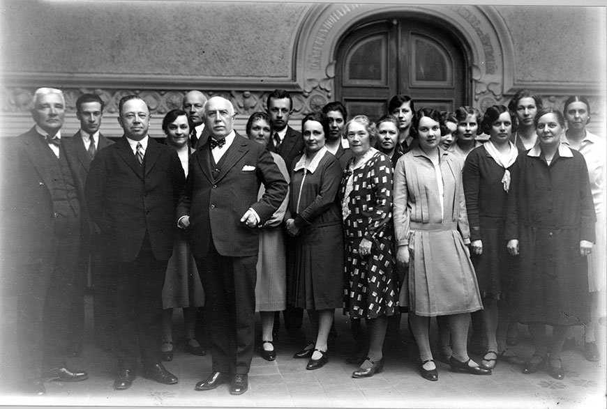 Joukko tullikamarin palveluksessa olleita siviilipukuisia miehiä ja naisia seisomassa Helsingin tullikamarirakennuksen aulassa 1930-luvun alussa.