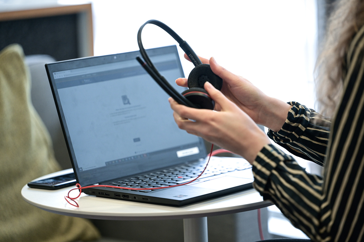 Nainen työpöydän ääressä tietokoneella kuulokkeet kädessä.