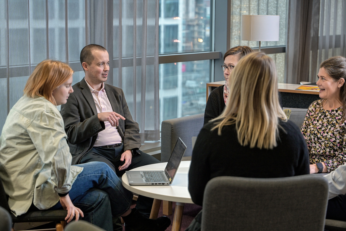 Viisi henkilöä istuu toimistolla pöydän ääressä ja keskustelee.