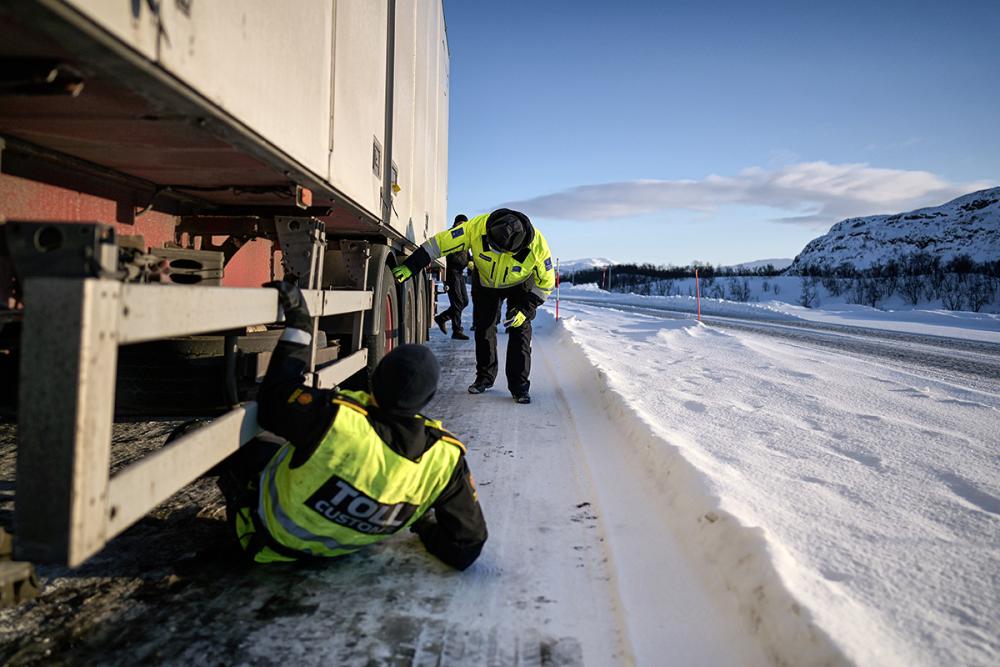 Norjalainen ja suomalainen tullitarkastaja tutkivat lumisessa maisemassa suurta rekkaa.