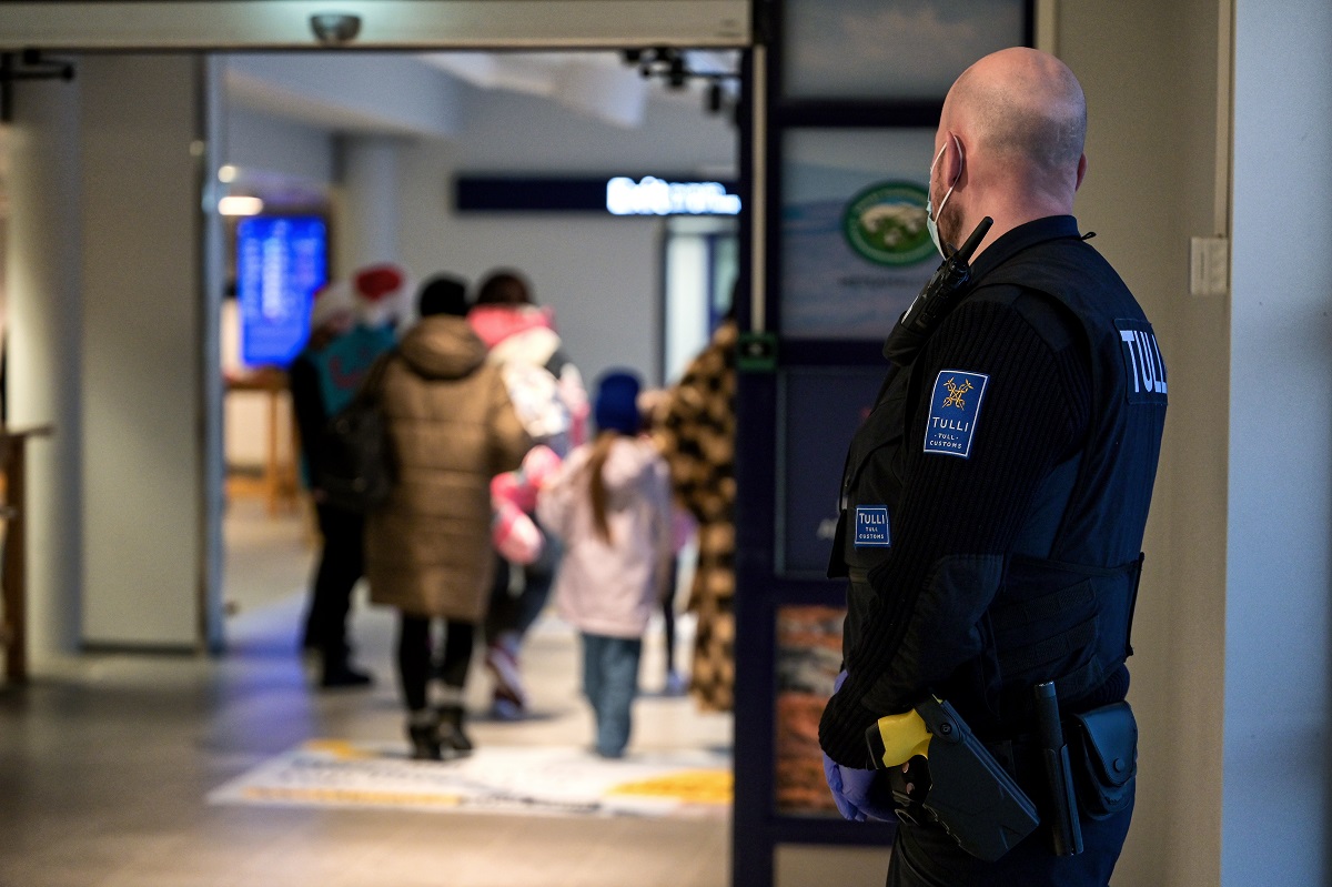 Tullinspektören följer resenärerna med blicken. Tullinspektören har ansiktsmask och skyddshandskar.
