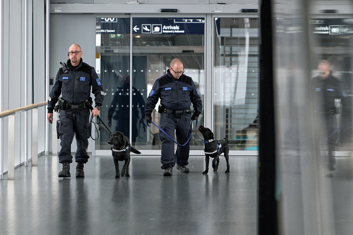 Kaksi tullivirkailijaa kahden mustan labradorinnoutajan kanssa lentoaseman käytävällä.